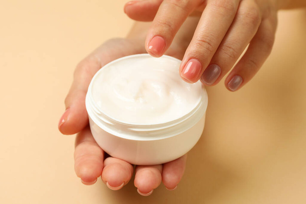 Cute female hands hold jar of cosmetic cream on beige background - Fotó, kép