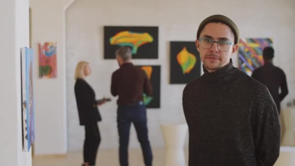 Πορτρέτο του νεαρού καυκάσιου άνδρα βλέποντας ζωγραφική στον τοίχο και στη συνέχεια κοιτάζοντας κάμερα και χαμογελώντας κατά την επίσκεψη γκαλερί τέχνης - Πλάνα, βίντεο