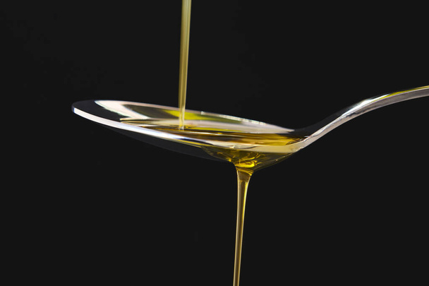 Olio d'oliva liquido su un cucchiaio su fondo nero. Cottura - Foto, immagini