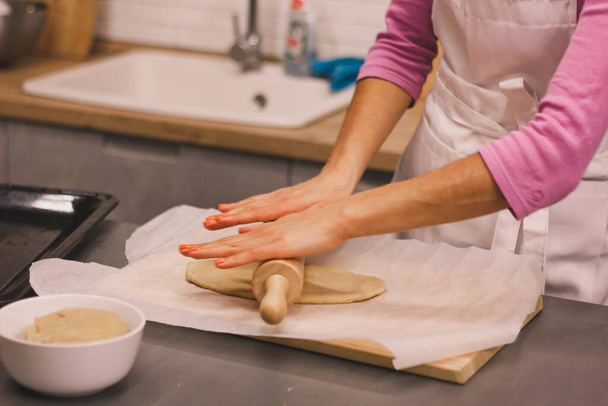 Hands work with the dough to make fresh ginger cookies. Women's hands make dough for homemade cookies on a wooden table, sprinkled with flour . Women's hands roll out the dough - Fotó, kép