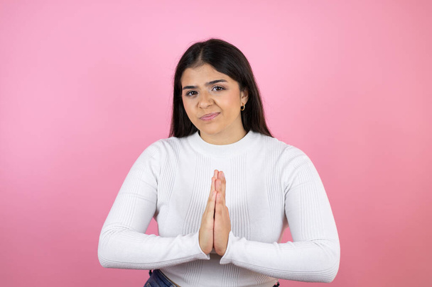 Young beautiful woman over isolated pink background begging and praying with hands together with hope expression on face very emotional and worried - Photo, Image