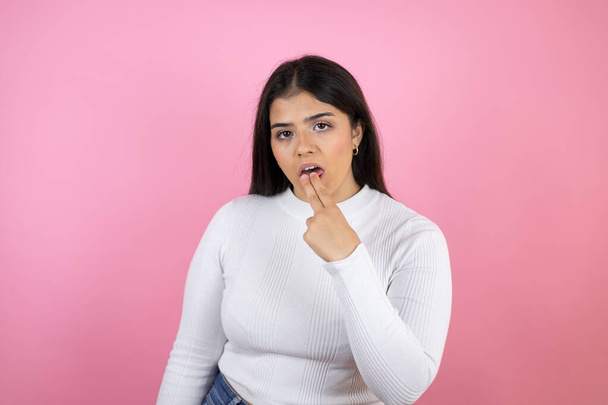 Young beautiful woman over isolated pink background disgusted with her hand inside her mouth - 写真・画像