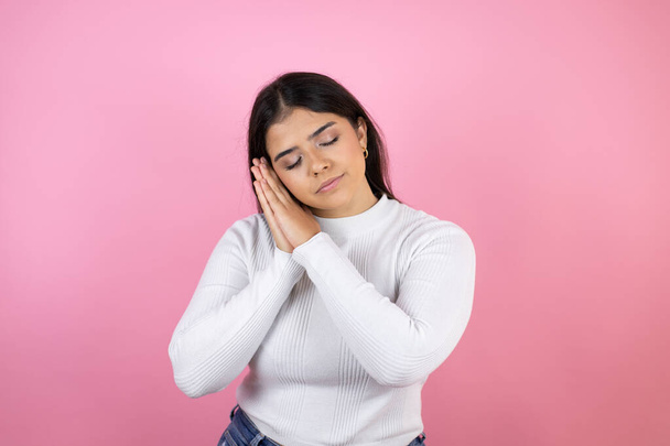 Young beautiful woman over isolated pink background sleeping tired dreaming and posing with hands together while smiling with closed eyes. - Foto, imagen