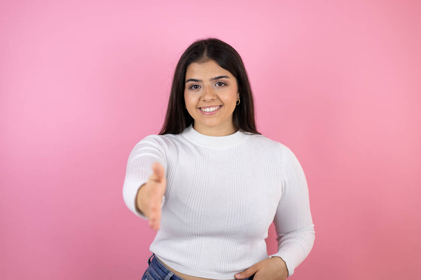 Молода красива жінка над ізольованим рожевим тлом посміхається дружній пропонує рукостискання як привітання і привітання
 - Фото, зображення