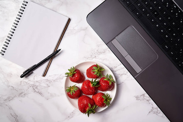 Open laptop computer, blank notebook with pen and strawberries on table, copy space. Freelancer workspace, home office. Top view, flat lay - Фото, изображение