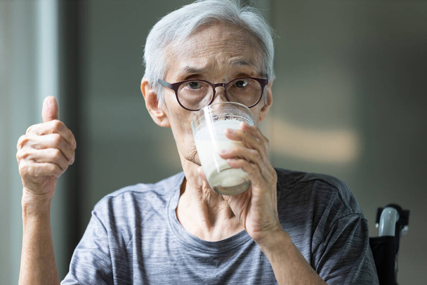 Asian senior woman drinking fresh milk from the glass,old elderly holding glass of milk,showing thumb up while drinking and looking at camera,health care,healthy nutrition,food and drinks concept - Photo, Image