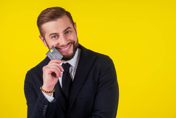 Portrait of handsome young businessman holding credit card over yellow background - Фото, изображение