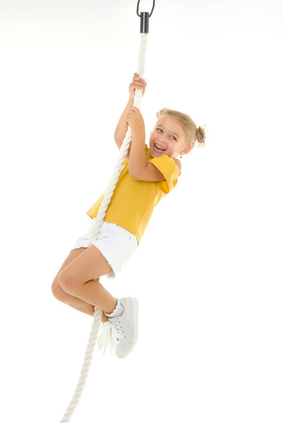 A little girl holds on to the rope with her hands, swinging on it. - Photo, Image