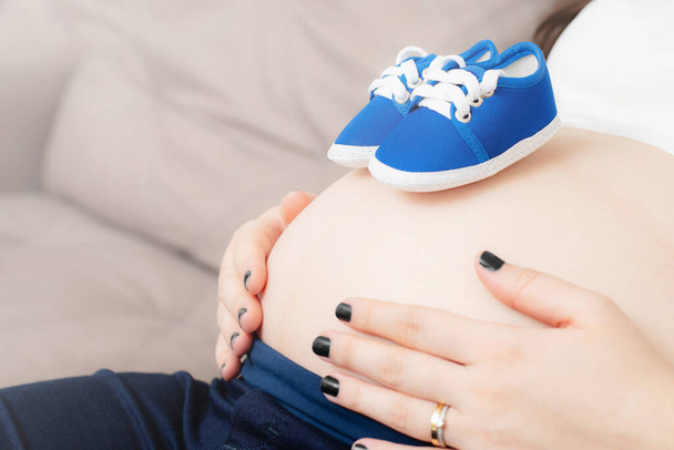 Zapatos de bebé en el vientre de una mujer embarazada. Es un niño. Mamá sosteniendo el vientre. - Foto, imagen
