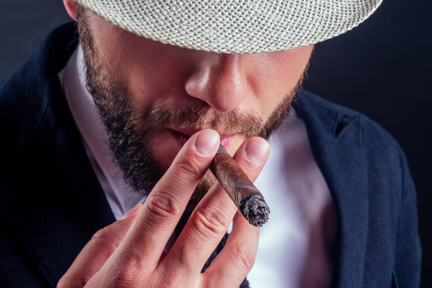 Porträt eines attraktiven Geschäftsmannes mit Zigarre im Studio mit schwarzem Hintergrund - Foto, Bild