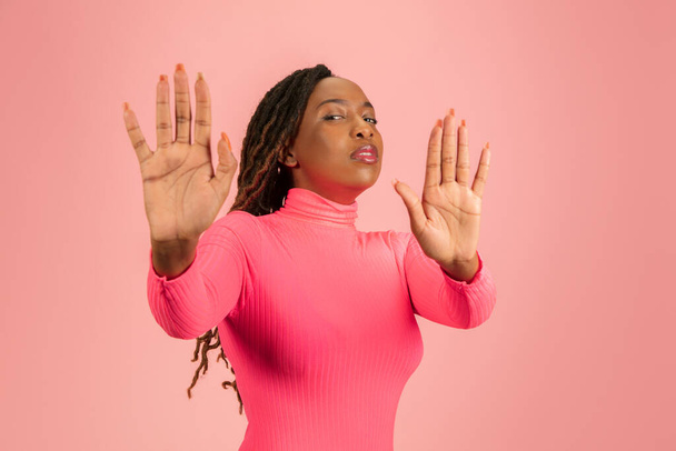 Retrato de una joven afroamericana aislada sobre fondo de estudio rosa, expresión facial. Hermoso retrato femenino de media longitud con copyspace. - Foto, imagen