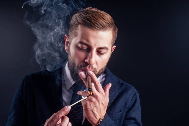 Portrait of an attractive business man with a cigar in black background studio - Fotoğraf, Görsel