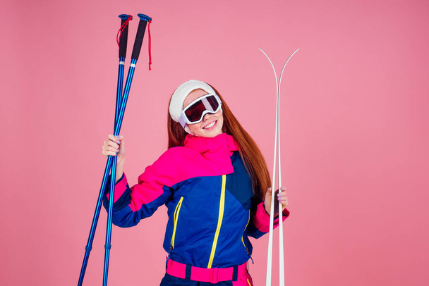 redhaired ginger young woman with skis posing in studio on pink background - Photo, Image