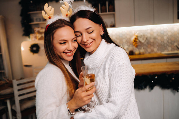 two girls in a cozy home environment with champagne in their hands at Christmas. Smiling girls drink champagne on a festive evening. - Fotografie, Obrázek