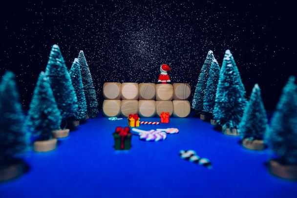 Weihnachtskomposition mit Tannenbäumen, Bonbons, Geschenken und kleinem Weihnachtsmannspielzeug, das im Hintergrund in den Nachthimmel blickt. Schnee und leuchtende Sterne. Kopierraum - Foto, Bild