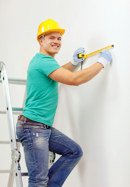 Smiling man in protective helmet measuring wall - Photo, image