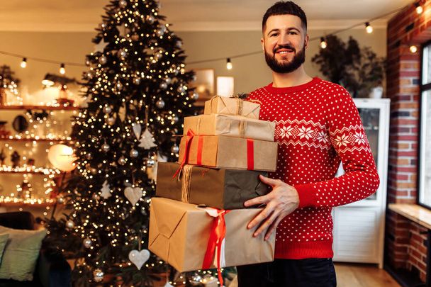 Happy young man in red New Year's sweater, with many gift boxes at home, Merry Christmas - Foto, afbeelding