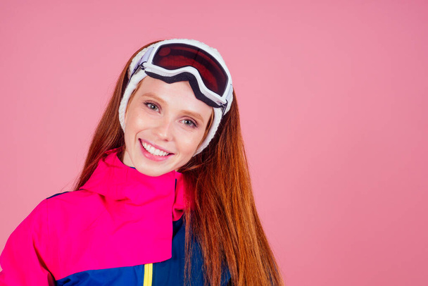 redhaired ginger young woman with skis posing in studio on pink background - Foto, afbeelding