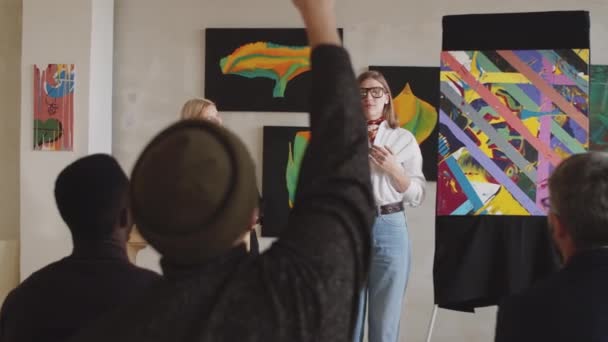 Νεαρή χαρούμενη γυναίκα καλλιτέχνης παρουσιάζει αφηρημένη ζωγραφική της στο κοινό και απαντώντας σε ερωτήσεις σε δημοπρασία τέχνης στην γκαλερί - Πλάνα, βίντεο