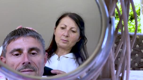 Taglio di capelli a casa. Parrucchiere femminile pettinando i capelli al marito con riflessi mrror - Filmati, video