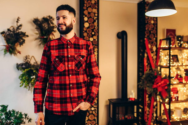 Christmas attractive young man, in a red shirt, celebrates Christmas at home, in a stylishly decorated house before Christmas, Merry Christmas and Happy New Year - Fotó, kép
