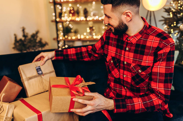 Happy young man opening Christmas gifts at home against the background of a decorated Christmas tree, Merry Christmas and New Year - Foto, Bild