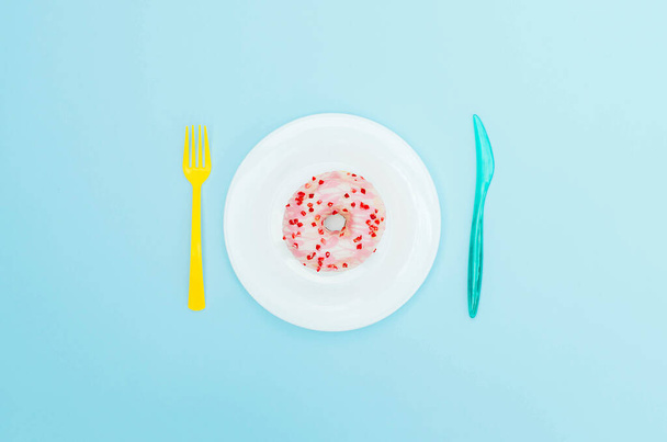 Rosado donut en un plato azul con cubiertos. - Foto, Imagen
