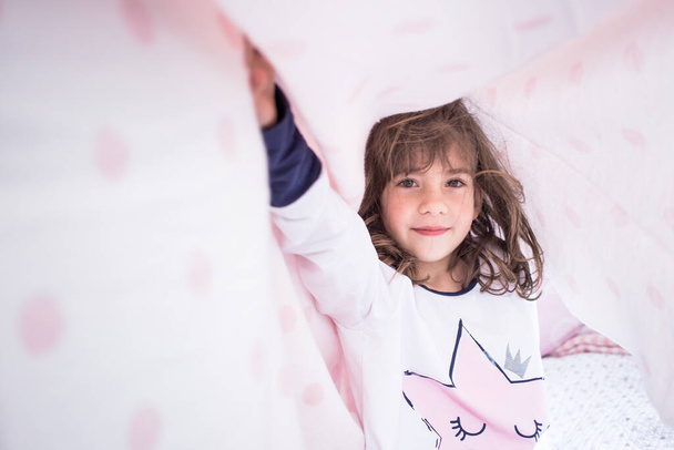 Little brunette girl playing on her bed in pajamas. - Fotó, kép