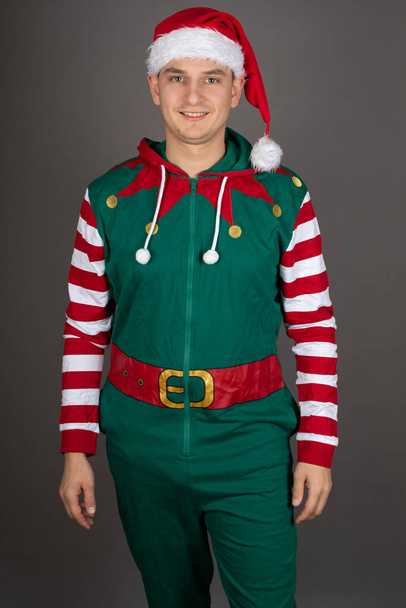 Portrait of handsome man wearing Grinch costume is smiling to the camera on grey background - Фото, зображення