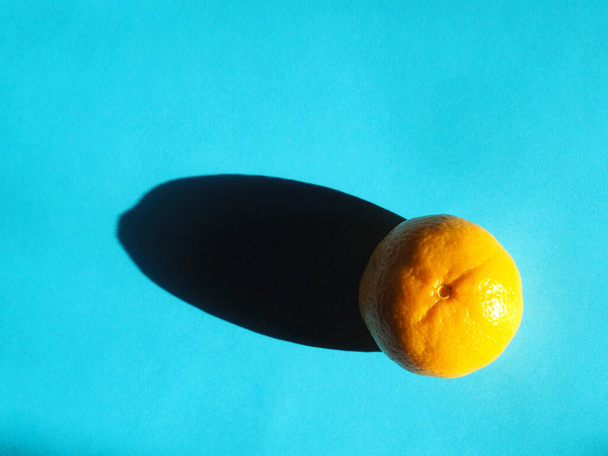 mandarina con una sombra dura sobre un fondo azul - Foto, imagen