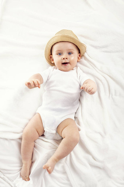 Cute baby boy smiling to the camera, lying on white background. Little kid wearing summer hat. Studio shot. - Foto, afbeelding