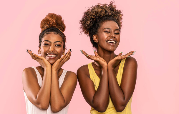 Happy overjoyed two afro women smile broadly, looking at camera, posing on pink pastel studio background.  - Fotoğraf, Görsel