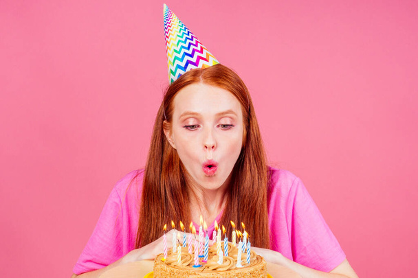 redhaired ginger woman make a wish fingers crossed , eyes closed blowing out candles on a birthday cake - Fotoğraf, Görsel