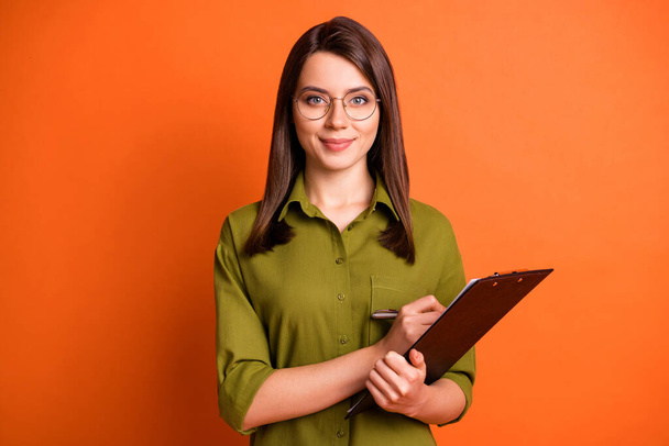Retrato fotográfico de una trabajadora que mantiene el portapapeles de la pluma en entrevistas sonriendo en gafas aisladas sobre un fondo de color naranja vivo - Foto, Imagen