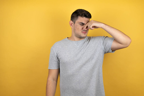 Young handsome man wearing a casual t-shirt over isolated yellow background Young handsome man wearing a casual t-shirt over isolated yellow background thinking looking tired and bored with hands on head - Photo, Image