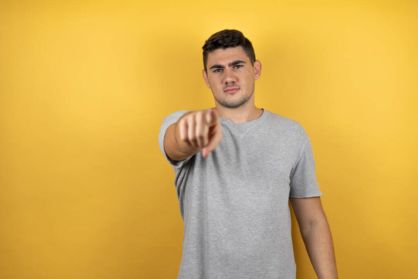 Junger gutaussehender Mann in einem lässigen T-Shirt über isoliertem gelben Hintergrund, der mit dem Finger nach vorne zeigt - Foto, Bild