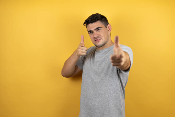 Young handsome man wearing a casual t-shirt over isolated yellow background pointing to you and the camera with fingers, smiling positive and cheerful - Photo, Image