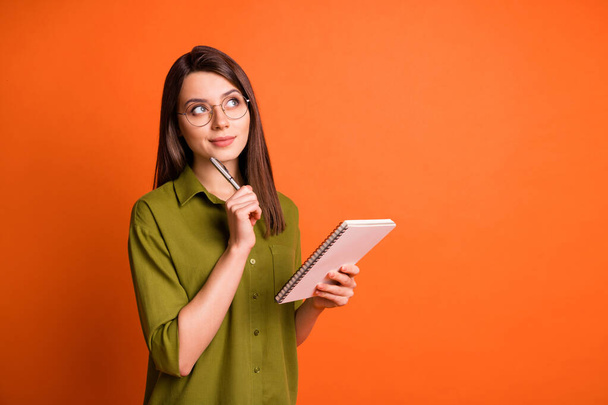 Photo portrait of thoughtful dreamy brunette girl writing with pen isolated on vivid orange color background - Fotó, kép