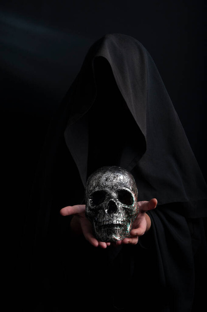 Hand hält einen menschlichen Schädel auf dunklem Hintergrund, eine symbolische Hommage an den Tod - Foto, Bild