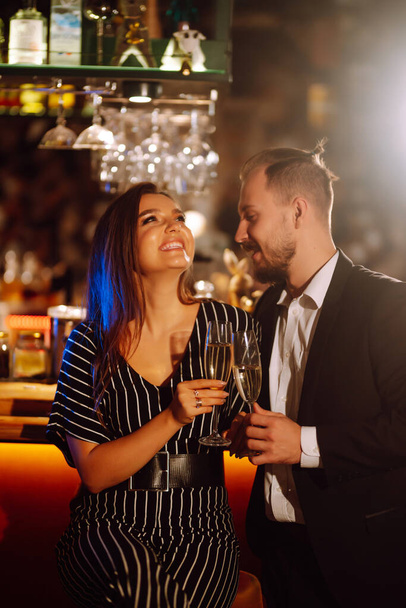 Happy loving couple enjoying having drinks together at the bar. Young man and woman clinking a glass champagne, enjoying winter holiday. Party, celebration, drink, birthday concept. Romantic evening. - Foto, afbeelding