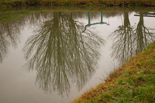 Reflection of the crowns of trees and swing on the water surface of the pond  - Foto, Bild