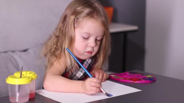 γοητευτικό μικρό ξανθό κορίτσι σε κόκκινο καρό φόρεμα, ζωγραφική με πολύχρωμα χρώματα. Παιδική ηλικία, τέχνη, μπογιά. FullHD πλάνα - Πλάνα, βίντεο