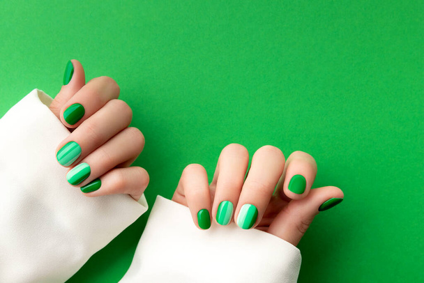 Schöne gepflegte Frauenhände mit Frühling-Sommer-Nageldesign auf grünem Hintergrund. Maniküre, Pediküre Schönheitssalon Konzept. Leerer Platz für Text - Foto, Bild