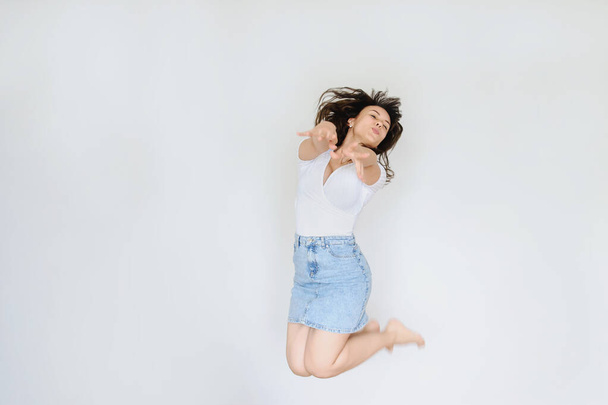 close up photo of a happy brunette in white blouse and denim skirt jumping in the air - Фото, изображение
