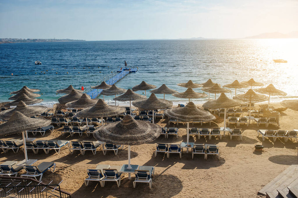Соломенные пляжные зонтики и шезлонги на пляже на идиллическом тропическом курорте для летнего отдыха - Фото, изображение