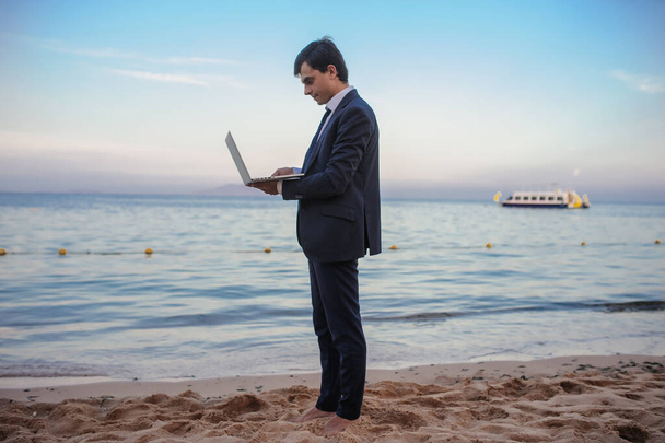 boczny widok młodego człowieka w garniturze z laptopem pracującego nad morzem - Zdjęcie, obraz