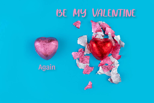 Concept of February 14 or Valentine's Day. Chocolate candy-a heart in a red wrapper and a torn wrapper from the candy, and pink bonbon. Light Blue background. Be my Valentine again. - Photo, image