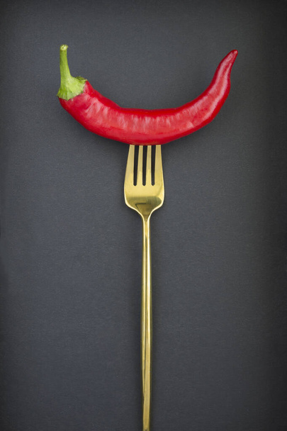 One chili  impaled on a gold fork on the black  background - 写真・画像