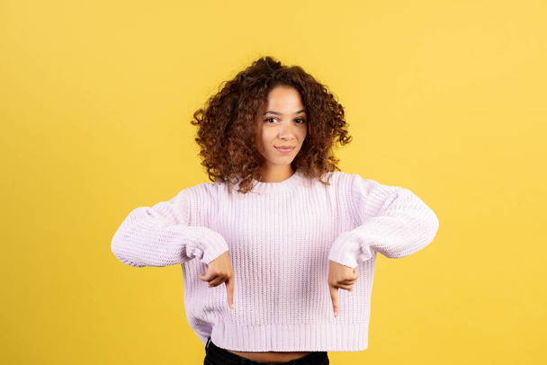 Here you find solution. Smiling, confident adult african american woman pointing down with fingers, showing good deal and offer, looking at camera, standing on yellow copy space background - Photo, Image