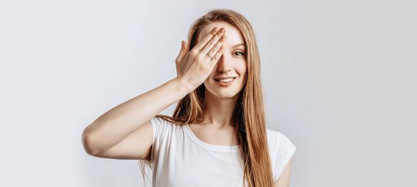 Young beautiful girl smiling and covering half of her face with hand on gray isolated background - Foto, Imagen